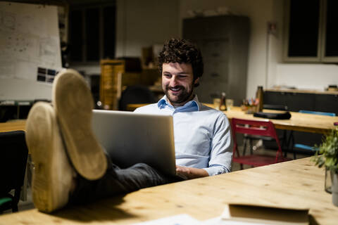 Geschäftsmann mit Laptop im Büro mit Füßen auf dem Schreibtisch, lizenzfreies Stockfoto