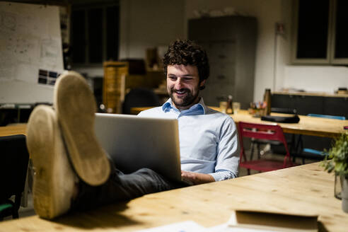 Geschäftsmann mit Laptop im Büro mit Füßen auf dem Schreibtisch - GIOF06766