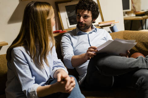 Geschäftsmann und Geschäftsfrau sitzen auf der Couch im Büro und besprechen Papiere, lizenzfreies Stockfoto