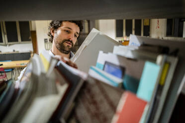 Geschäftsmann beim Lesen von Akten in einem Regal im Büro - GIOF06850