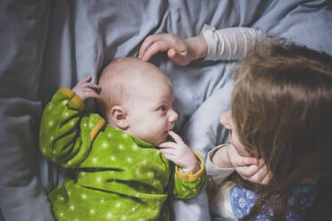 Little girl lying on bed playing with baby girl, top view - IHF00176