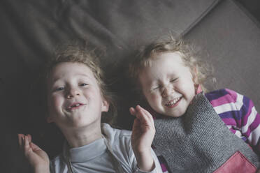 Portrait of two little sisters lying side by side on couch having fun, top view - IHF00179