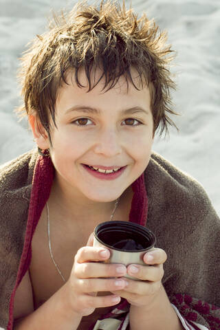 Porträt eines lächelnden Jungen, der sich nach dem Schwimmen mit einer Tasse Tee wärmt, lizenzfreies Stockfoto