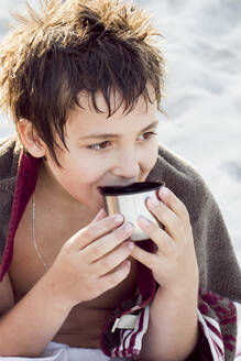 Porträt eines Jungen, der sich nach dem Schwimmen mit einer Tasse Tee aufwärmt - IHF00188