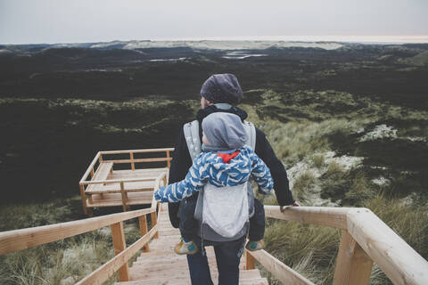 Rückenansicht eines Mannes mit Kleinkind im Kinderwagen auf dem Rücken vor einer Aussichtsterrasse, Sylt, Deutschland, lizenzfreies Stockfoto