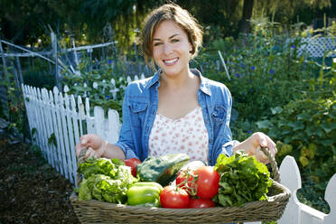 Gemischtrassige Frau hält Korb mit Gemüse im Garten - BLEF10531