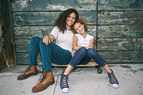Gemischtrassige Mutter und Tochter sitzen auf einem Skateboard, lizenzfreies Stockfoto