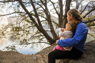 Caucasian mother and daughter sitting at lake - BLEF10614