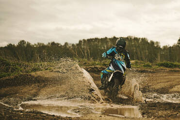 Caucasian man riding dirt bike in puddle - BLEF10641