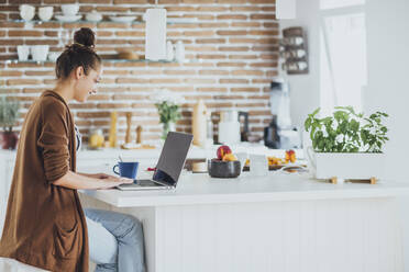 Caucasian woman using laptop in kitchen - BLEF10747