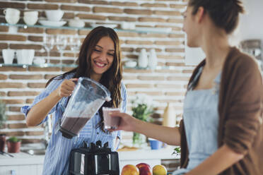 Caucasian women pouring smoothie in kitchen - BLEF10749