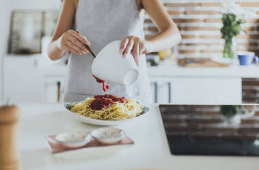 Caucasian woman pouring sauce on pasta in kitchen - BLEF10758