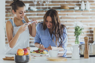 Caucasian women photographing pasta in kitchen - BLEF10759