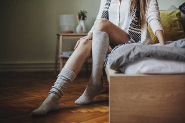 Kaukasische Frau sitzt auf dem Bett und trägt Socken - BLEF10770