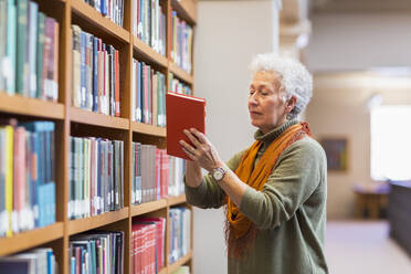 Older mixed race woman choosing book in library - BLEF10827