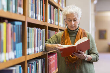 Ältere gemischtrassige Frau liest ein Buch in der Bibliothek - BLEF10829