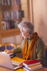 Ältere gemischtrassige Frau schreibt in der Bibliothek - BLEF10835