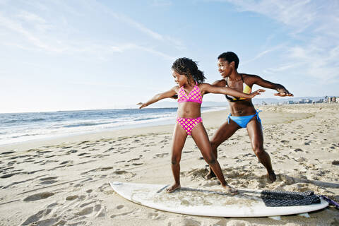 Schwarze Mutter bringt ihrer Tochter am Strand das Surfen bei, lizenzfreies Stockfoto