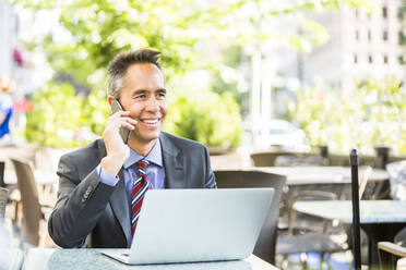 Mixed race businessman talking on cell phone in cafe - BLEF10957