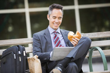 Mixed race businessman eating and using digital tablet - BLEF10961