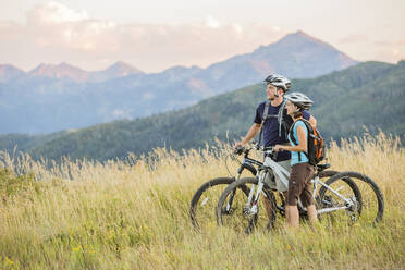 Caucasian couple riding mountain bikes in field - BLEF10982