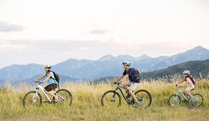 Kaukasische Familie fährt Mountainbike auf einem Feld - BLEF10984
