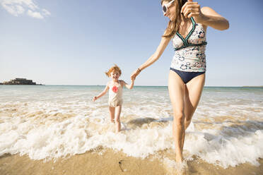 Caucasian mother and daughter playing in waves on beach - BLEF11002
