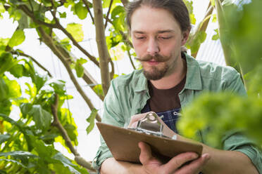 Caucasian gardener writing on clipboard in greenhouse - BLEF11014