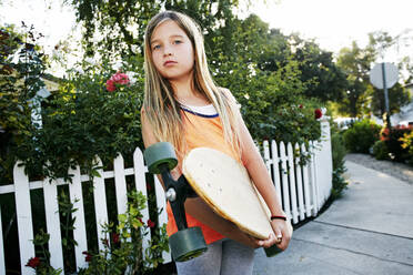 Kaukasisches Mädchen hält Skateboard auf dem Gehweg - BLEF11063