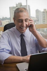 Hispanischer Geschäftsmann benutzt Handy und Laptop im Büro - BLEF11101