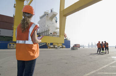 Frau mit Schutzhelm und Klemmbrett am Hafen stehend - BLEF11113