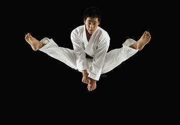 Asiatischer männlicher Karate-Schwarzgurt, der in die Luft tritt - BLEF11137