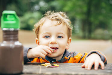 Kaukasischer Junge isst Snack am Picknicktisch - BLEF11195