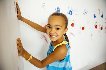 Mixed race girl making hand prints on wall - BLEF11208