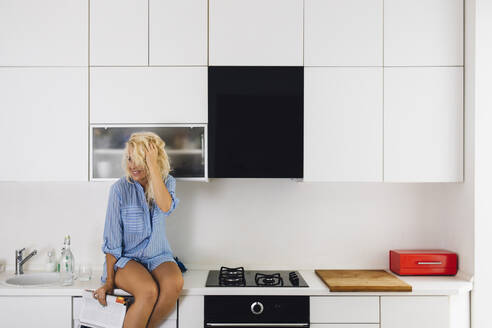 Woman sitting on kitchen counter - BLEF11299