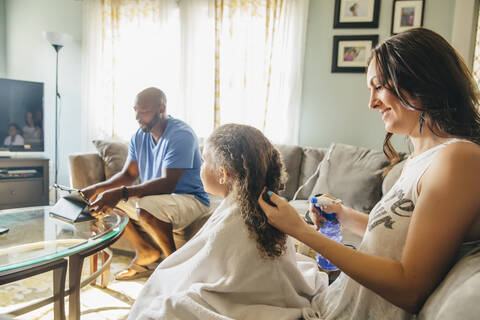 Mutter stylt Haare für Tochter im Wohnzimmer, lizenzfreies Stockfoto