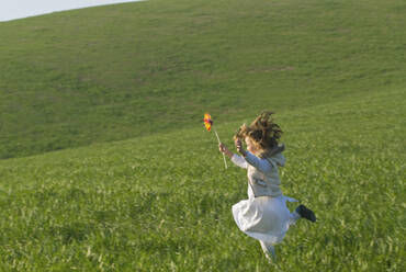 Young girl with wind wheel running in green fields - BLEF11413