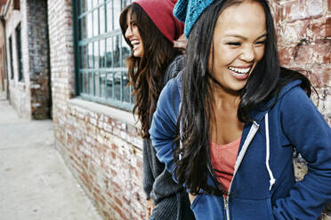 Women laughing in front of brick wall - BLEF11452