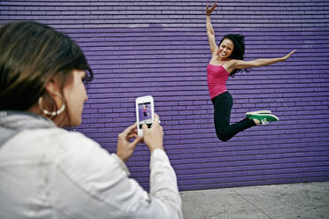 Woman photographing friend jumping for joy - BLEF11460