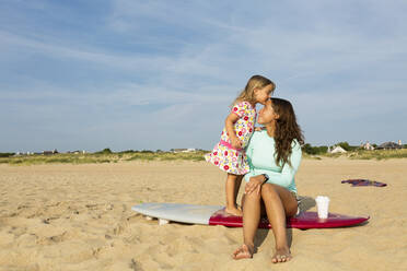 Mädchen küsst Stirn der Mutter auf Surfbrett am Strand - BLEF11513