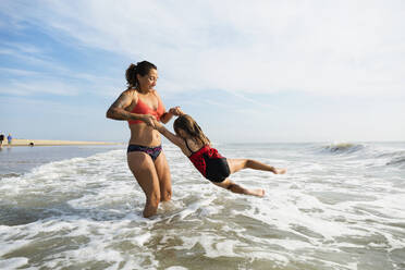 Mother and daughter playing in waves on beach - BLEF11522