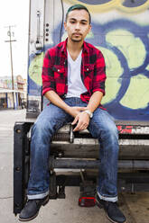 Hispanic man sitting on graffiti truck - BLEF11588