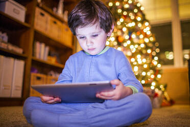 Kaukasischer Junge mit digitalem Tablet am Weihnachtsbaum - BLEF11592