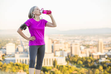 Caucasian woman drinking water bottle on urban hilltop - BLEF11638