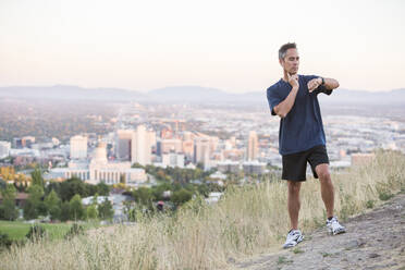 Gemischtrassiger Mann prüft den Puls auf einem Hügel über Salt Lake City, Utah, Vereinigte Staaten - BLEF11642