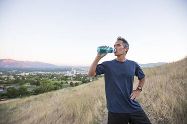 Mixed race man drinking water bottle on hilltop - BLEF11644
