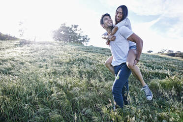 Man carrying girlfriend piggyback in field - BLEF11674