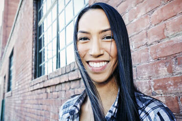 Mixed race woman smiling at brick wall - BLEF11709