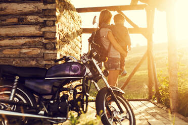 Mother holding son near motorcycle on patio - BLEF11807