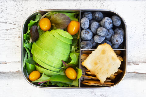 lunchbox/prep meal (gemischter grüner Salat mit Avocado und gelben Tomaten, Cracker, Blaubeeren, Salatsauce), Holzgabel, (alles ohne Platik), lizenzfreies Stockfoto